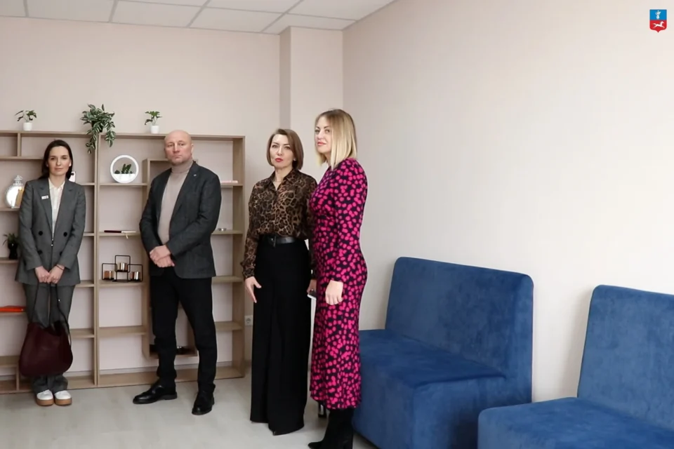 Чотири посадовці стоять у кімнаті притулку біля полиць і синіх диванів